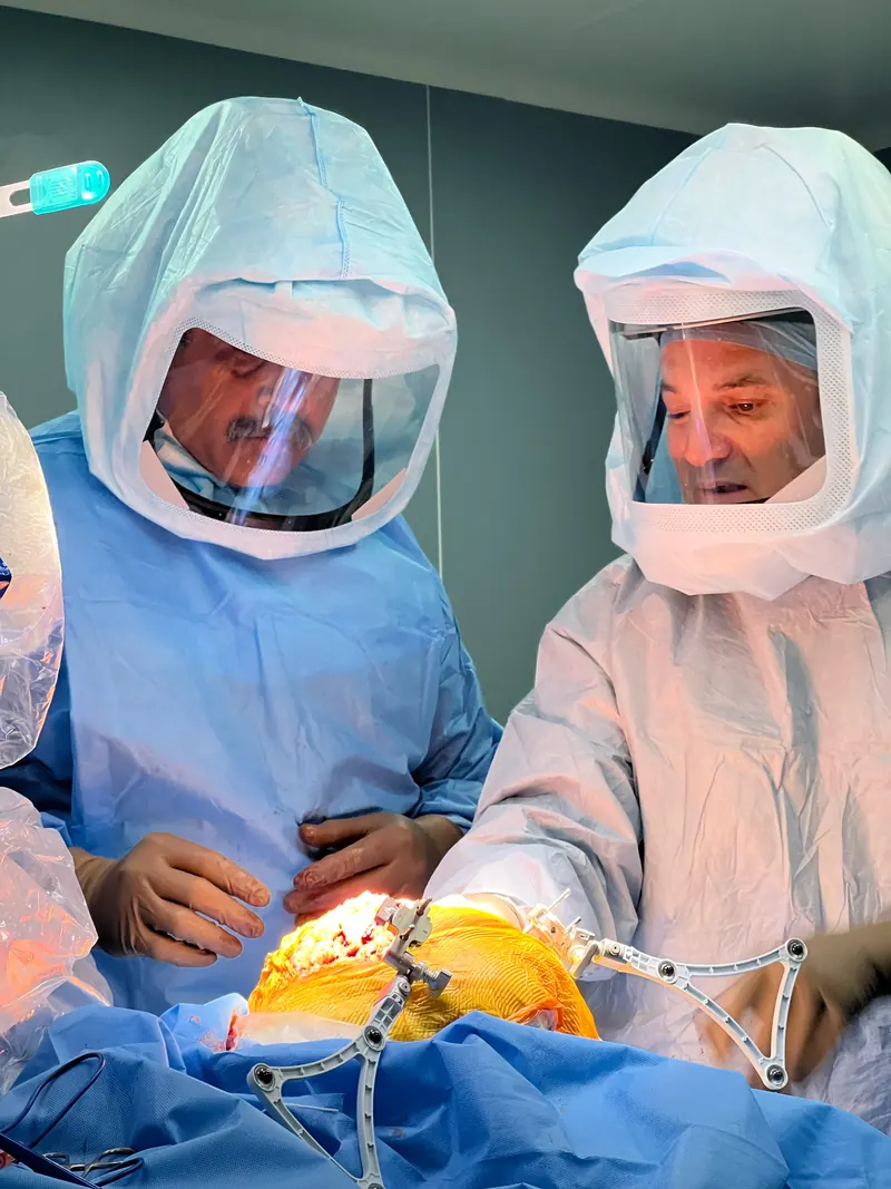 Surgeons in surgical helmets operating on a knee with robotic tracking arrays attached